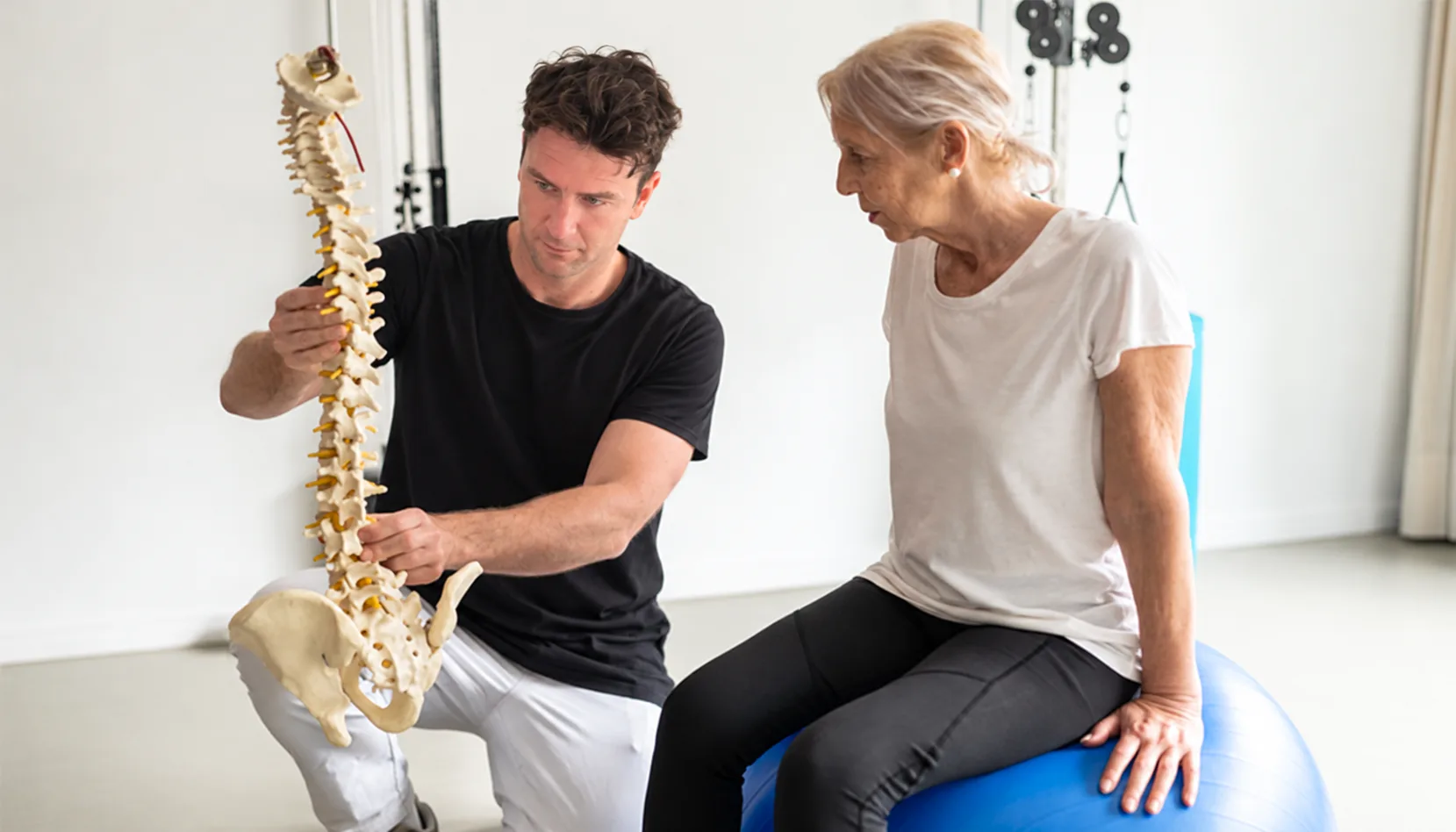 Practitioner showing a spine model to a patient seated on an exercise ball